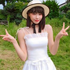 a woman in a white dress and hat posing for the camera with her hands up