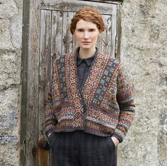 a woman standing in front of an old door wearing a sweater and pants with pockets