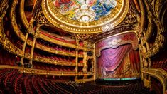 an ornate clock on the ceiling of a theatre with red curtains and gold trimmings