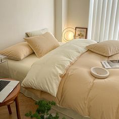 a laptop computer sitting on top of a bed next to pillows and pillowcases