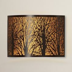 a lamp that is hanging on the wall in front of a window with trees silhouettes