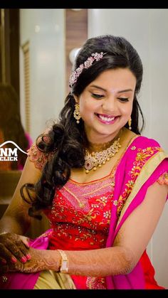 a woman in a red and gold sari smiles as she puts on her jewelry