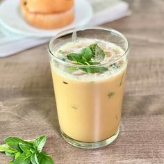 a glass filled with liquid sitting on top of a table next to a muffin