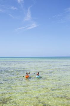 two people in kayaks paddling on the ocean with clear blue skies above them