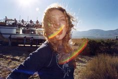 a woman with curly hair standing in front of a boat on the beach and smiling at the camera