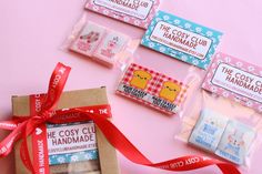 four packaged candy bars with red ribbon tied around them on a pink surface next to some packaging