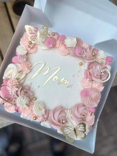 a mother's day cake with pink and white flowers in a gift box on a table