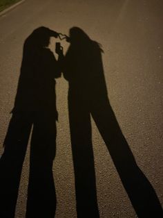 two people standing next to each other in the middle of a street with their shadow on the ground