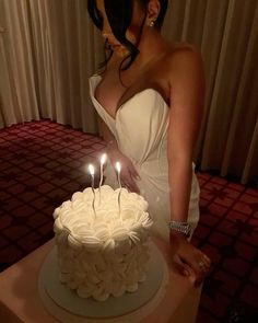 a woman is standing in front of a white cake with three candles on it,