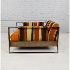 an orange and brown striped couch sitting on top of a white floor next to a brick wall