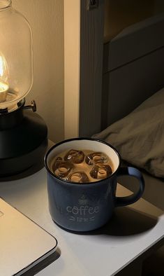 a cup of coffee sitting on top of a table next to a laptop and lamp