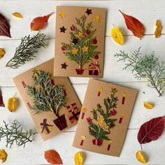 three cards with christmas trees on them surrounded by autumn leaves and other things to make it look like they are made out of cardboard