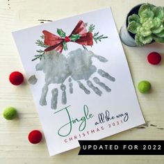 a christmas card with a handprint of a sheep and holly wreath on it next to some green balls