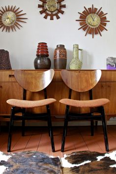 two chairs sitting next to each other in front of a dresser with clocks on the wall