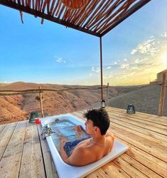 a man sitting in a hot tub on top of a wooden deck