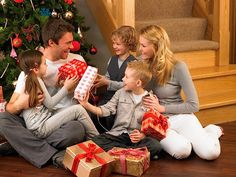 a family sitting on the floor with presents in front of a christmas tree