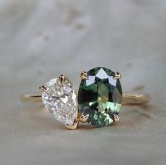 two engagement rings with an oval cut green and white diamond in the center, on a beige background