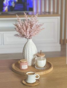 a white vase with some pink flowers in it on a tray next to a cup