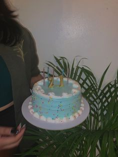 a woman holding a cake with candles in the shape of numbers on it and palm leaves