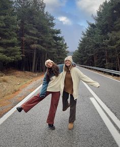 two women standing on the side of a road with their arms outstretched in front of them