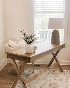 a wooden table sitting in front of a window next to a vase with flowers on it