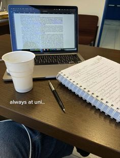 an open laptop computer sitting on top of a wooden desk next to a cup of coffee