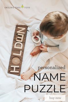 a small child sitting on top of a bed next to a wooden sign that says, personalized name puzzle