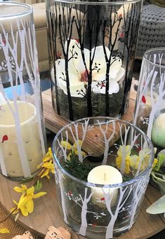 three candles sitting on top of a wooden table next to some flowers and trees in glass vases