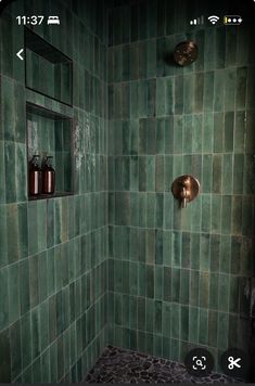 a green tiled shower with two soap dispensers on the wall next to it