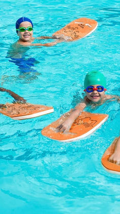 three children in swimming goggles are on surfboards and float around the pool water