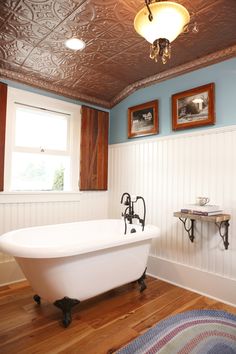 a bath tub sitting under a window next to a rug and two pictures on the wall