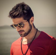 a man wearing sunglasses looking at his cell phone near the water with an ocean in the background