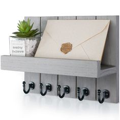 a wooden coat rack with hooks and an envelope on it next to a potted plant