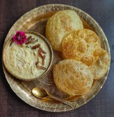 some food is on a silver plate with a spoon and flower in the bowl next to it