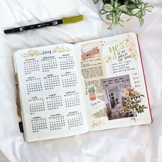 an open planner book sitting on top of a bed next to a potted plant