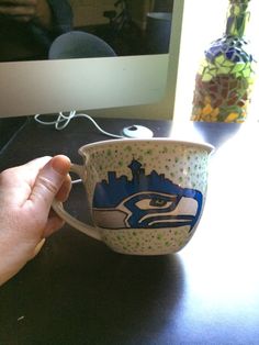 a hand holding a coffee cup with an eagle design on the bottom and side, in front of a computer screen