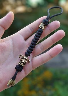 a hand holding a black rope with gold skulls on it and a skull head charm attached to the end