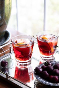 two glasses filled with liquid and cherries on a tray