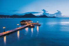 a pier at night with lights on it and mountains in the background