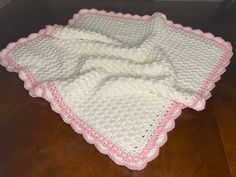 a white and pink crocheted blanket on top of a wooden floor next to a wall