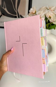 a person holding up a pink binder with the word't'written on it