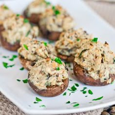 several stuffed mushrooms on a white plate with parsley sprinkled around the edges