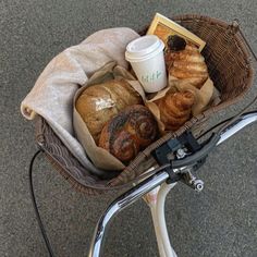 a basket filled with bread and pastries next to a cup of coffee on top of a bike