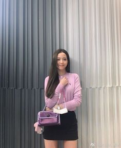 a woman holding a purple purse standing next to a metal wall with her hands in her pockets