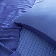 a bed with blue sheets and pillows on top of it, next to a pillow