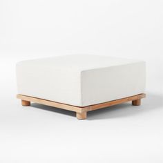 a white ottoman sitting on top of a wooden frame with no legs and an upholstered cushion