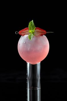 a pink drink with strawberries and mint garnish in a glass on a black background