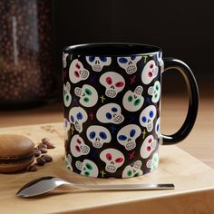 a black coffee mug with skulls on it next to a spoon and some beans in the background