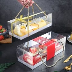 two clear boxes with strawberries, bananas and other fruit in them sitting on a table