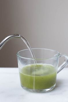 a glass filled with green liquid next to an apple